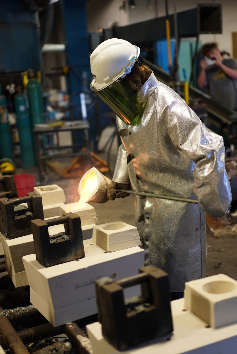 A student pouring metal into a mold.